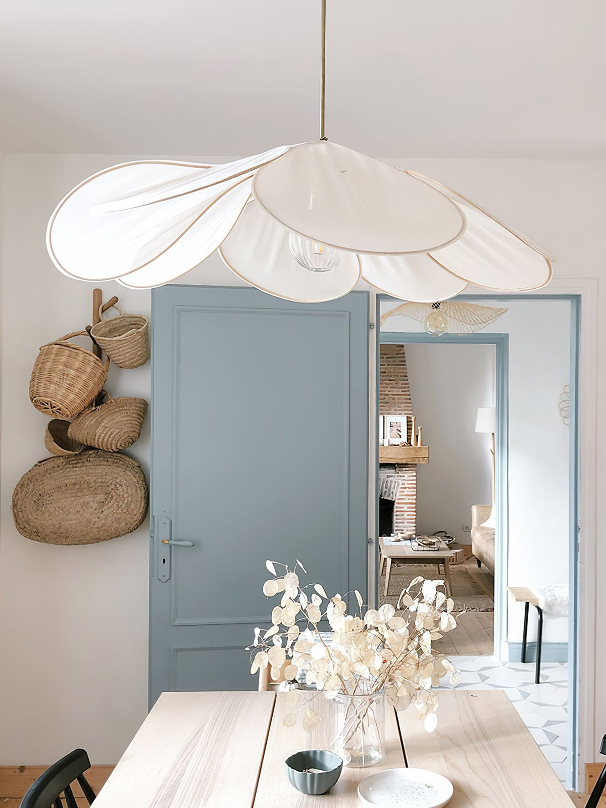 This Clérachic pendant lamp in white petals hangs near a blue door, above a wooden table set with white flowers.