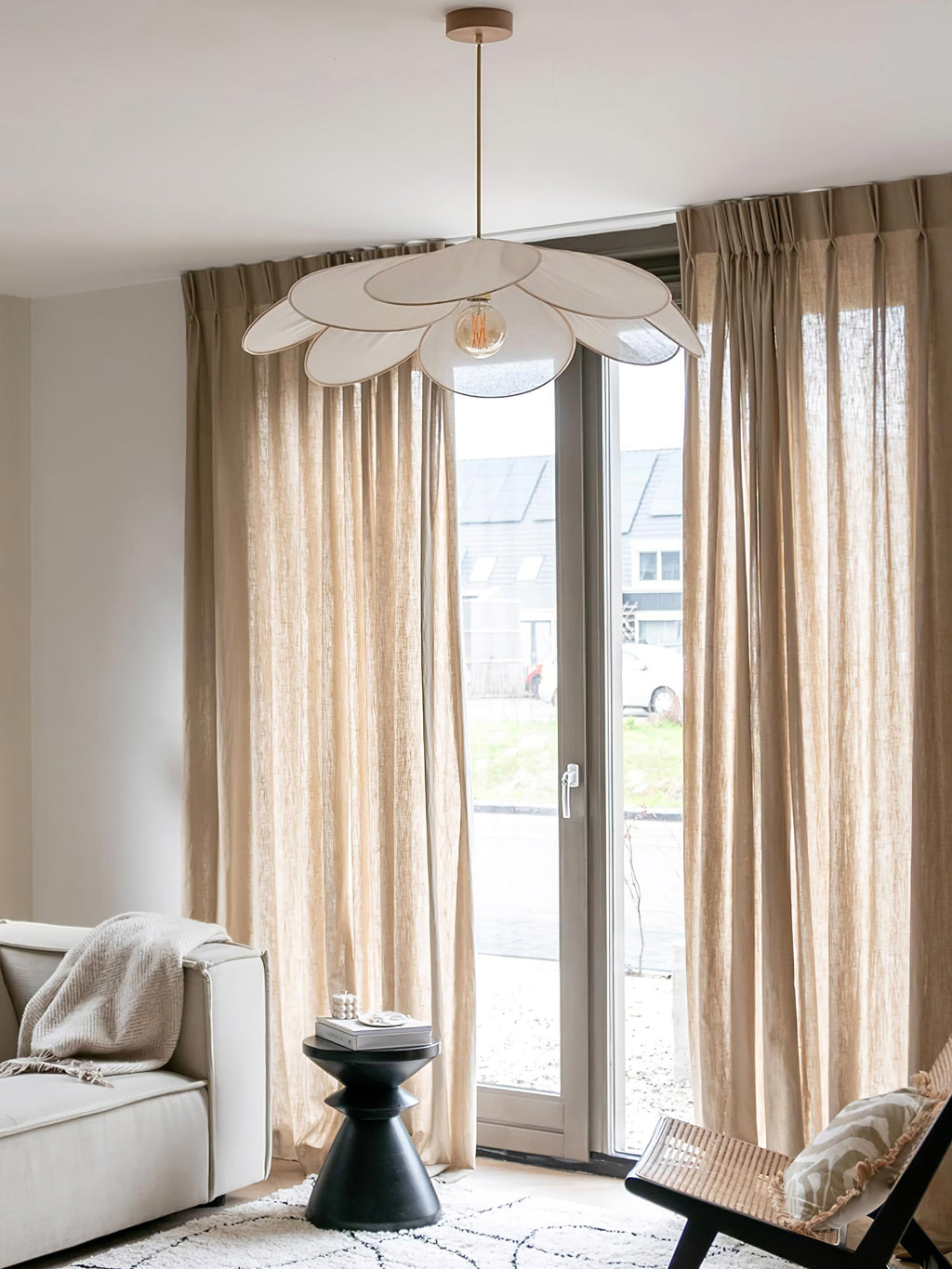 This Clérachic pendant lamp in white petals hangs in a living room with tan curtains and a white sofa beside glass doors.