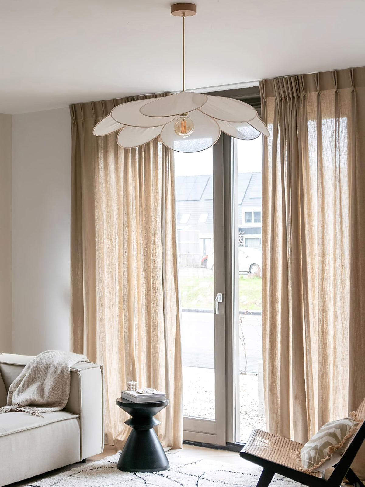 This Clérachic pendant lamp in white petals hangs in a living room with tan curtains and a white sofa beside glass doors.