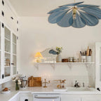 This Clérachic pendant lamp in a dusty-blue version hangs in a white kitchen with open shelving and a glass-front cabinet.