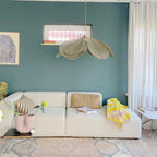 This Clérachic pendant lamp in a khaki-toned version hangs against a teal wall, above a beige sofa with striped cushions.