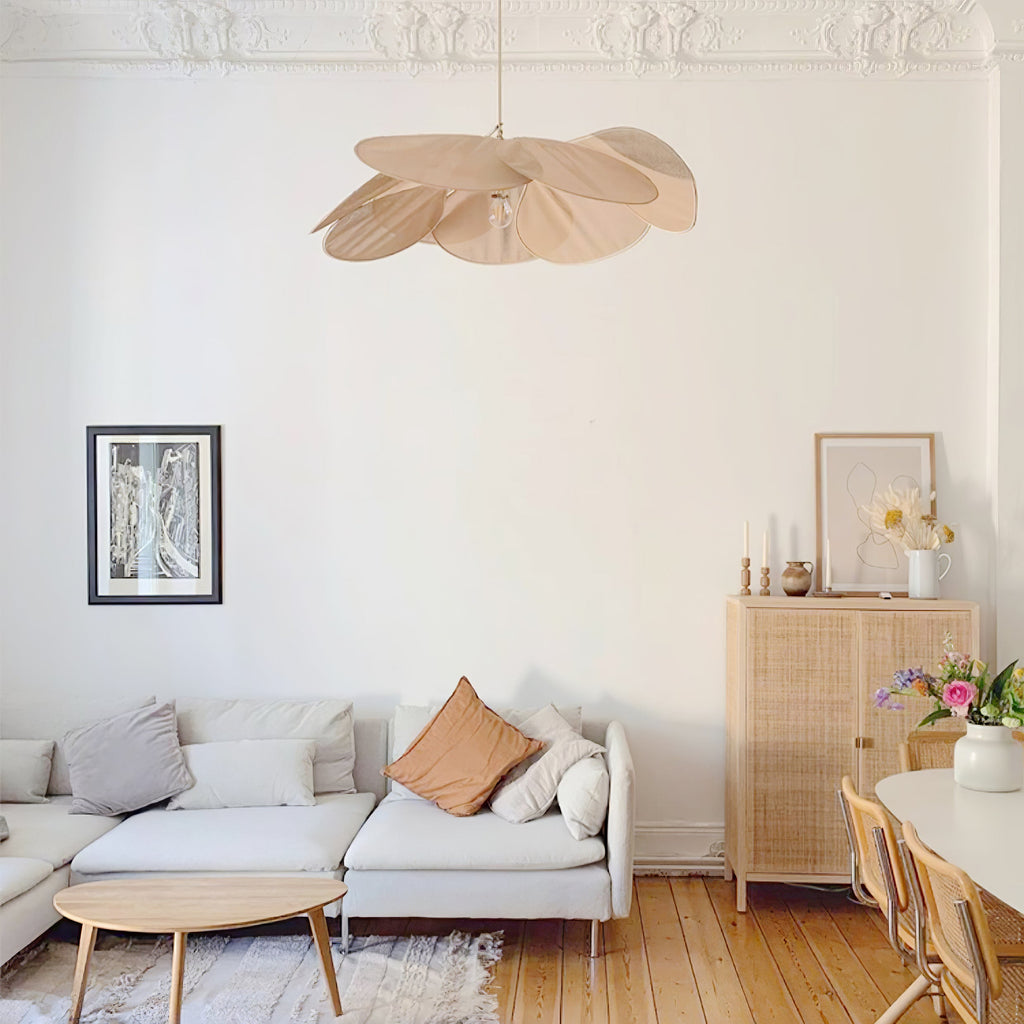 This Clérachic pendant lamp in tan petals hangs in a living room with a grey corner sofa and a rattan sideboard.