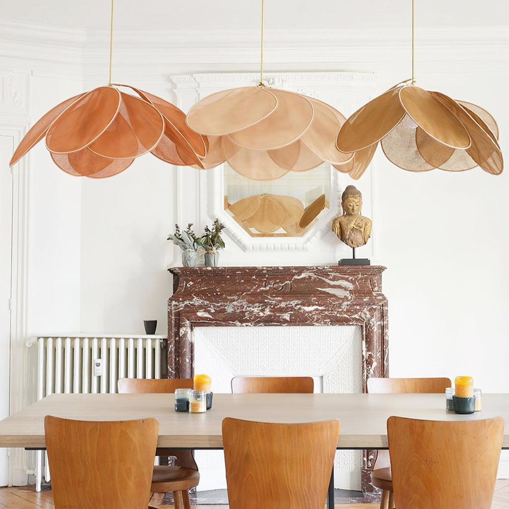 Three of these Clérachic pendant lamps in terracotta, beige and mustard fabric petals hang in a row above a dining table below a marble fireplace.