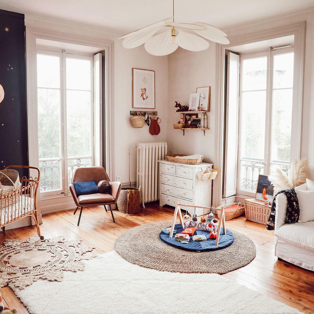 This Clérachic pendant lamp in cream fabric petals hangs in a child's room beside tall windows, with a cot and round rug below.