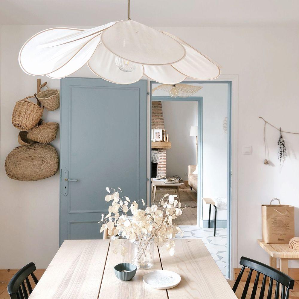 This Clérachic pendant lamp in cream fabric petals hangs above a wooden dining table in a hallway with a pale blue door.