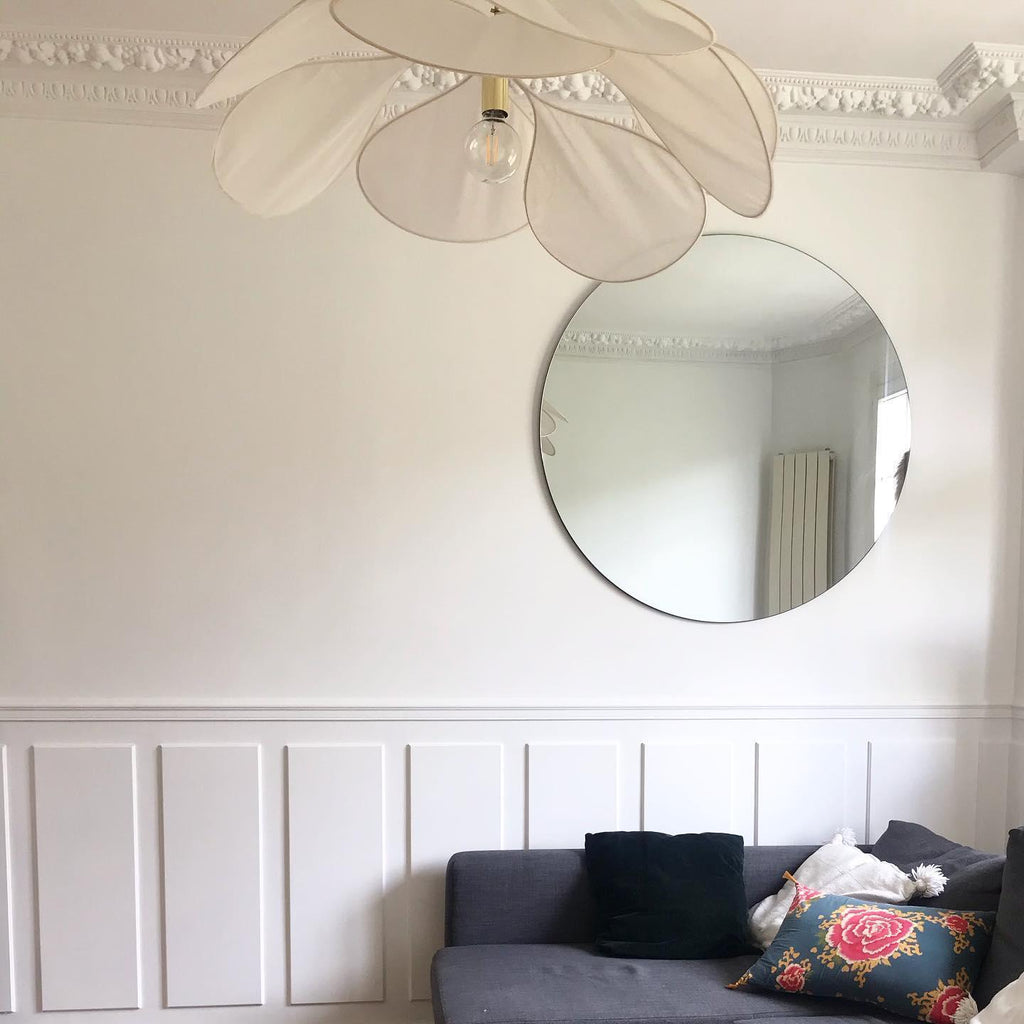 Close view of this Clérachic pendant lamp's cream fabric petals and bare bulb, hanging near a round wall mirror.