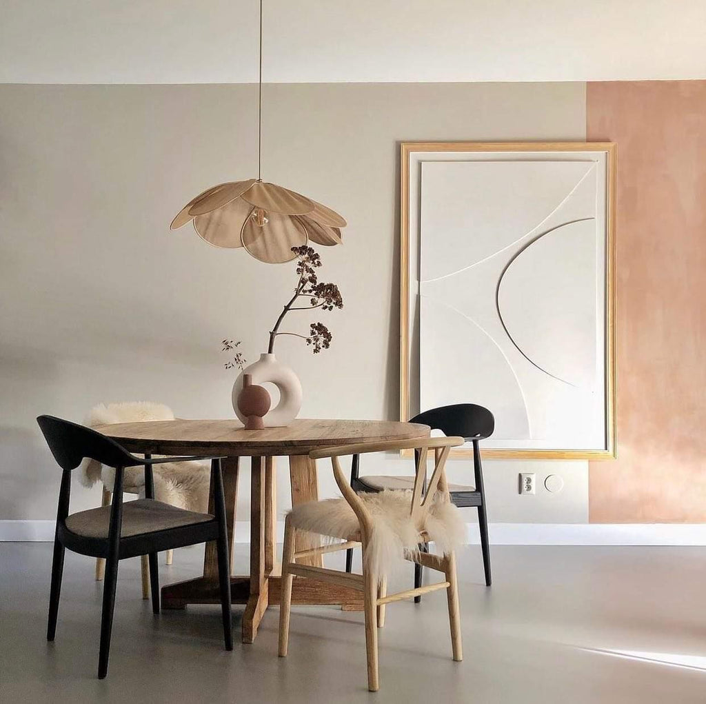 This Clérachic pendant lamp in warm tan petals hangs above a round wooden dining table beside a framed abstract print.