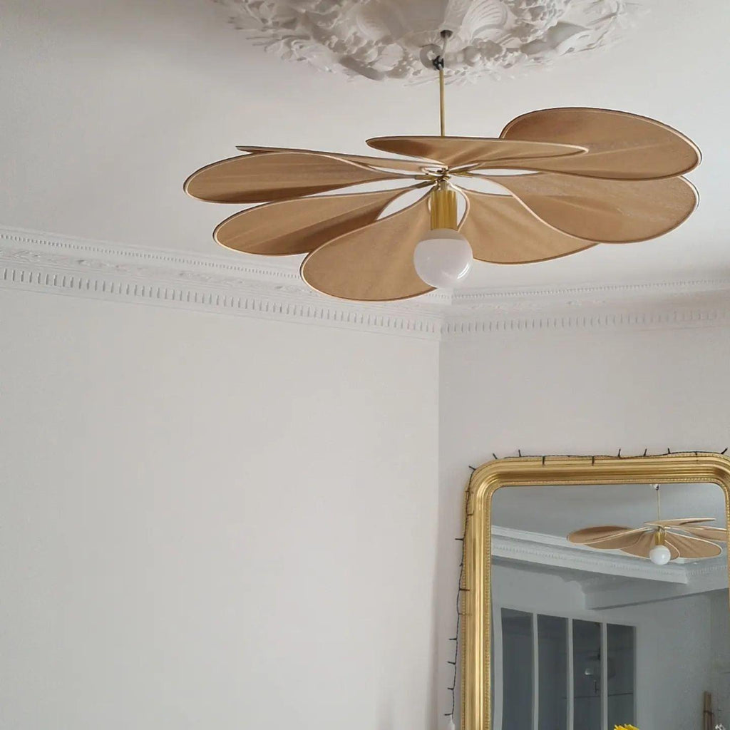 This Clérachic pendant lamp in tan petals hangs from an ornate ceiling rose, its bulb glowing beneath the fanned shade.