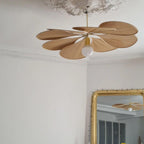 This Clérachic pendant lamp in tan petals hangs from an ornate ceiling rose, its bulb glowing beneath the fanned shade.