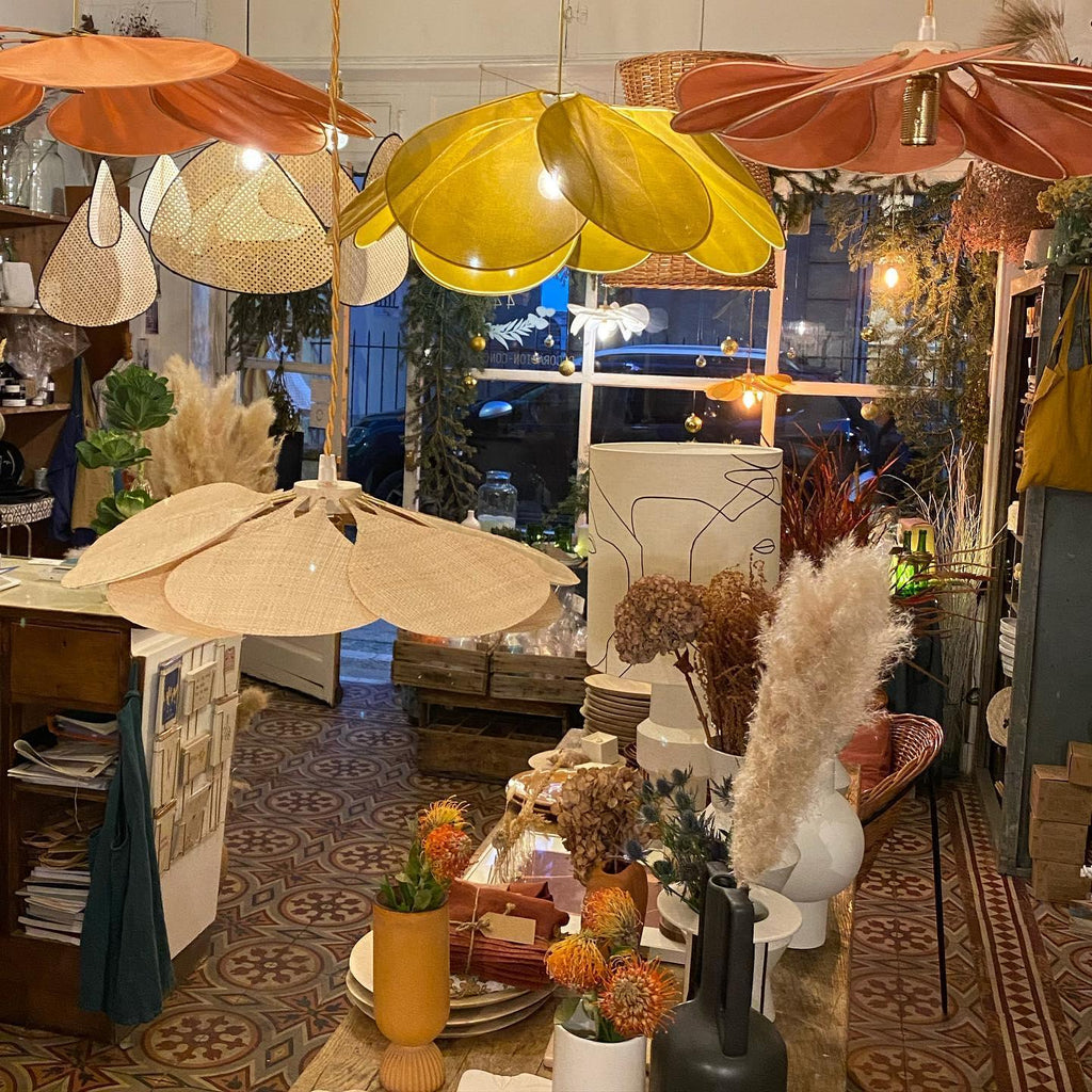 Multiple Clérachic pendant lamps in different fabric-petal colourways hang together in a plant-filled shop display strung with fairy lights.