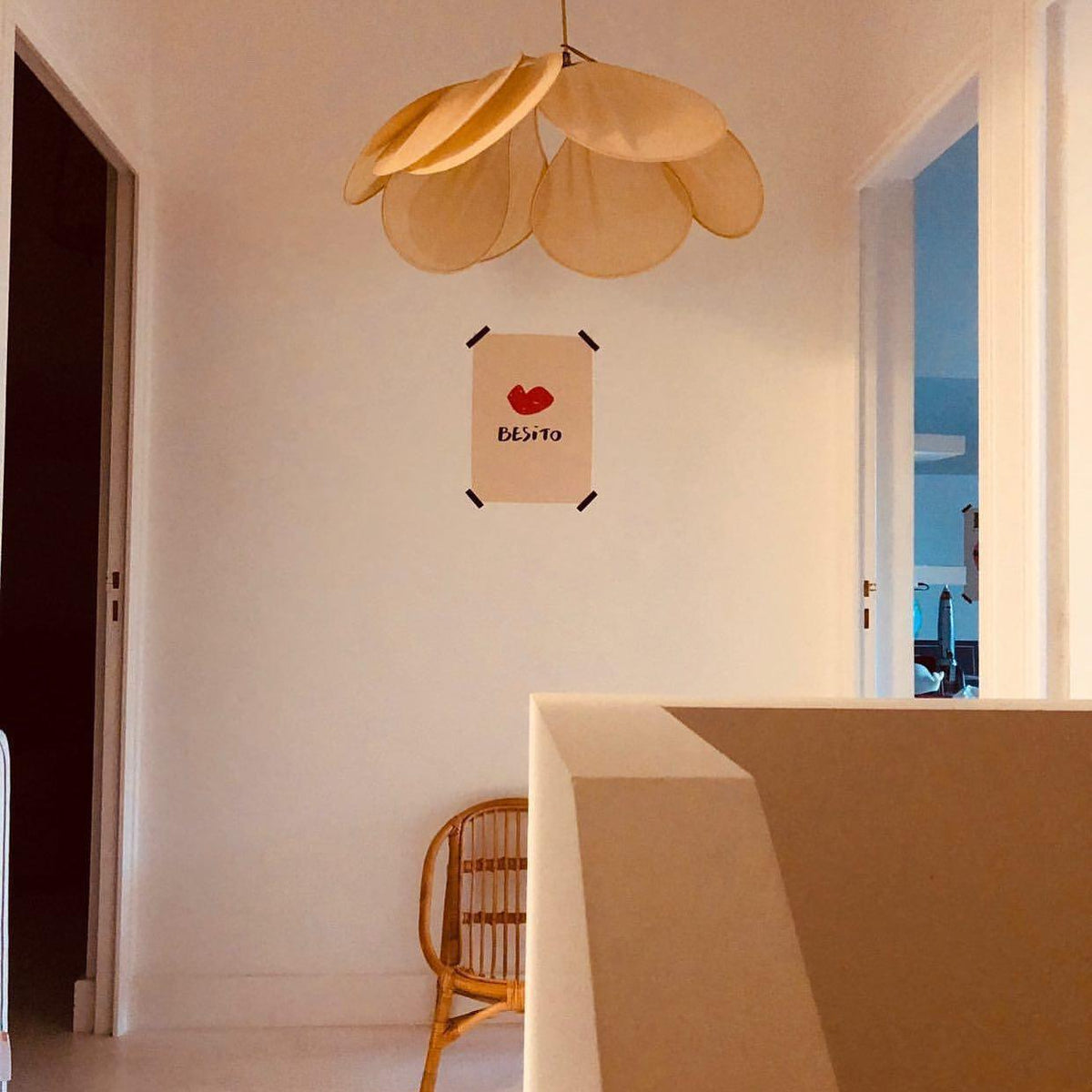 This Clérachic pendant lamp in tan petals hangs in a corner nook with blush-pink walls and a rattan chair.