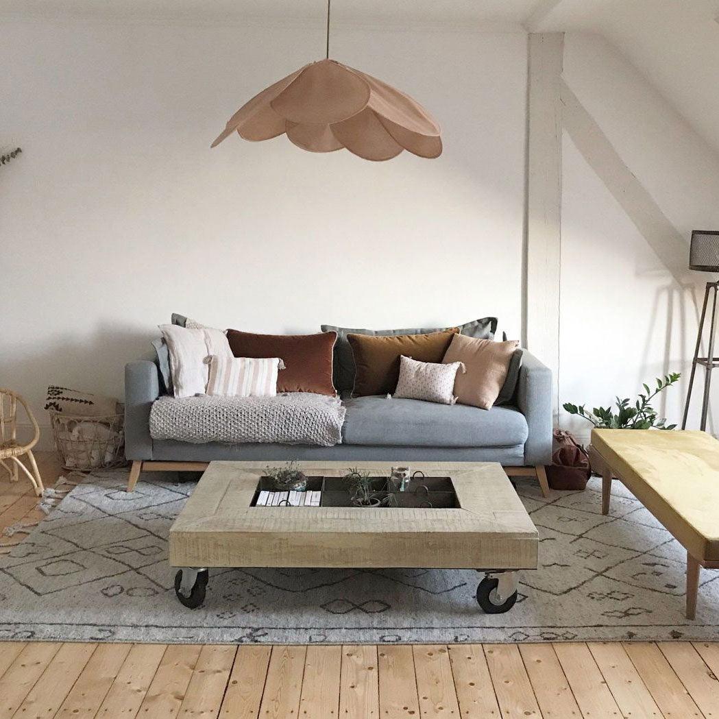 This Clérachic pendant lamp in blush-tan petals hangs beneath a sloped ceiling above a grey sofa and coffee table.