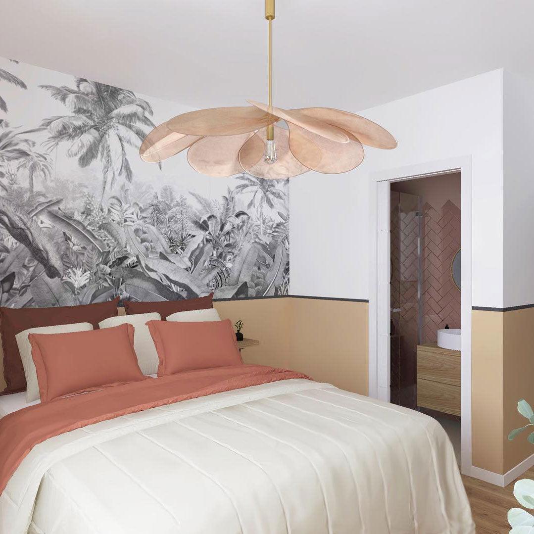 This Clérachic pendant lamp in tan petals hangs above a bed dressed in blush pink linens, beside a black-and-white palm-print wall.