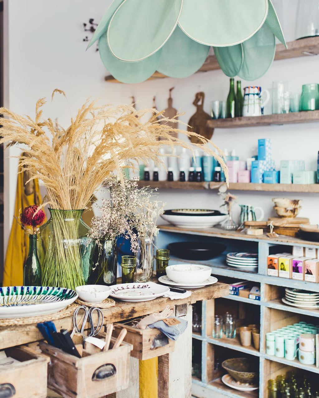 This Clérachic pendant lamp in a sage-green version hangs above open kitchen shelving stocked with glassware and dried pampas grass.