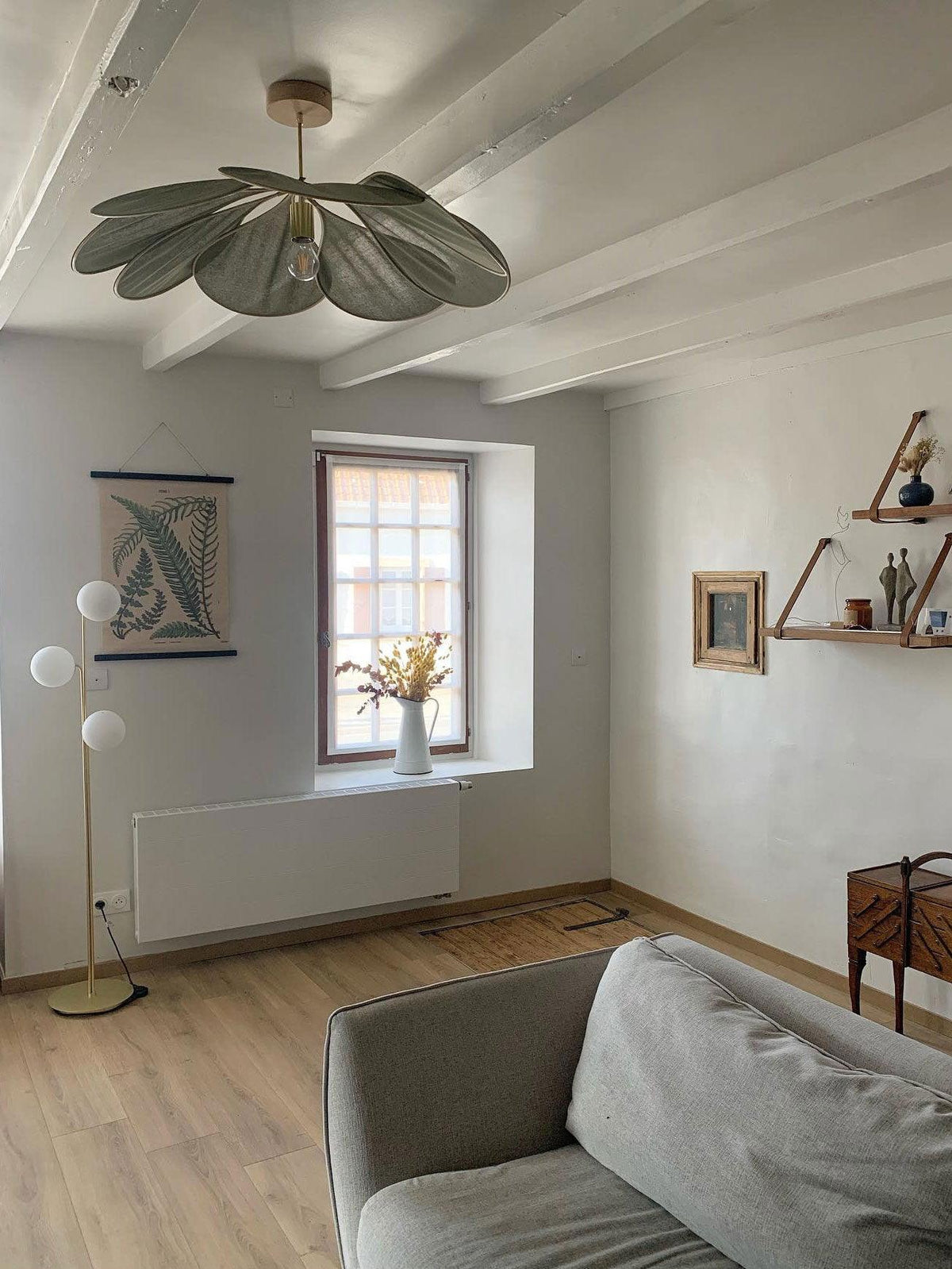 This Clérachic pendant lamp in a sage-green version hangs from a beamed ceiling in a room with a floor lamp and framed artwork.