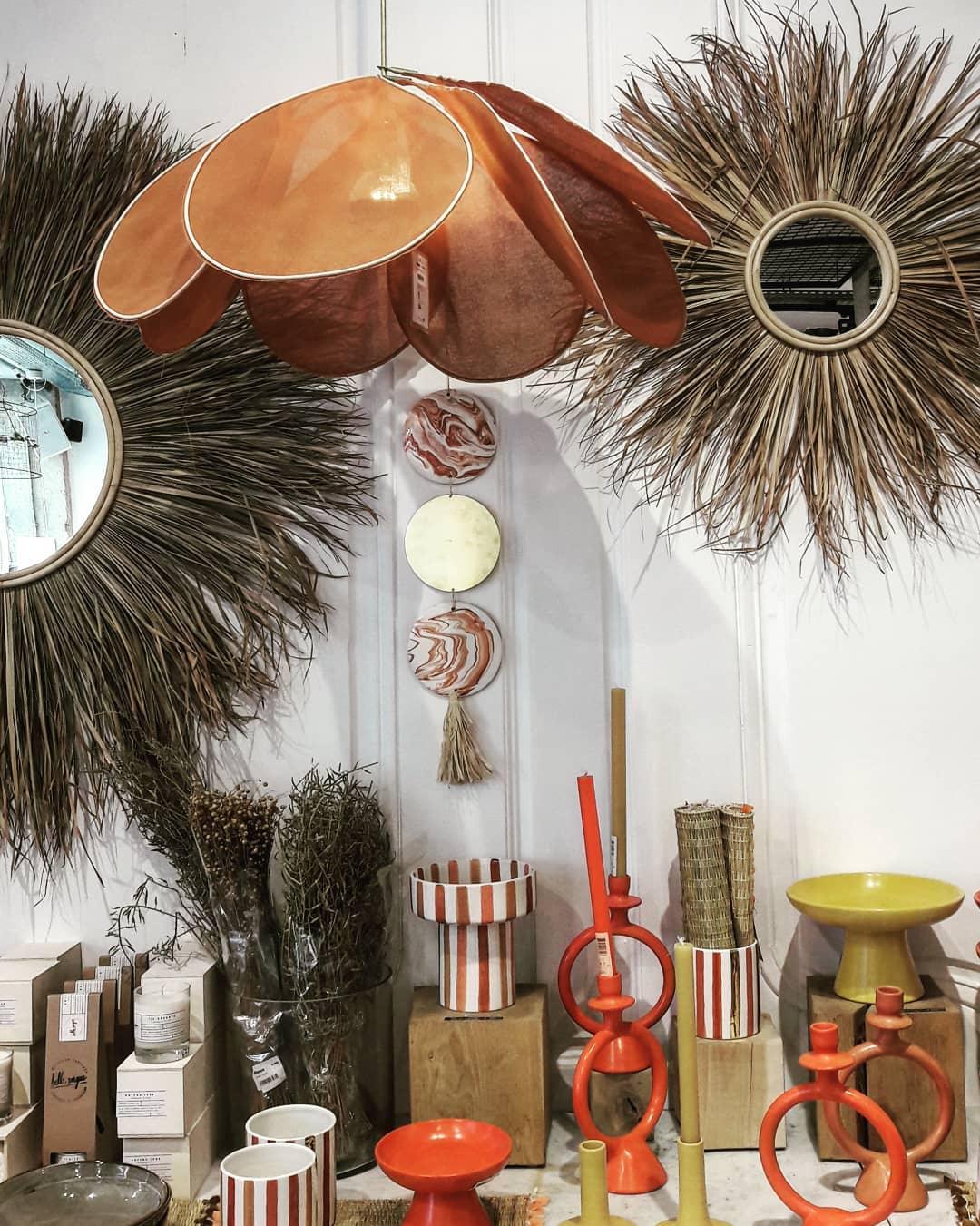 This Clérachic pendant lamp in copper-toned petals hangs between two sunburst straw mirrors in a home-decor shop display.