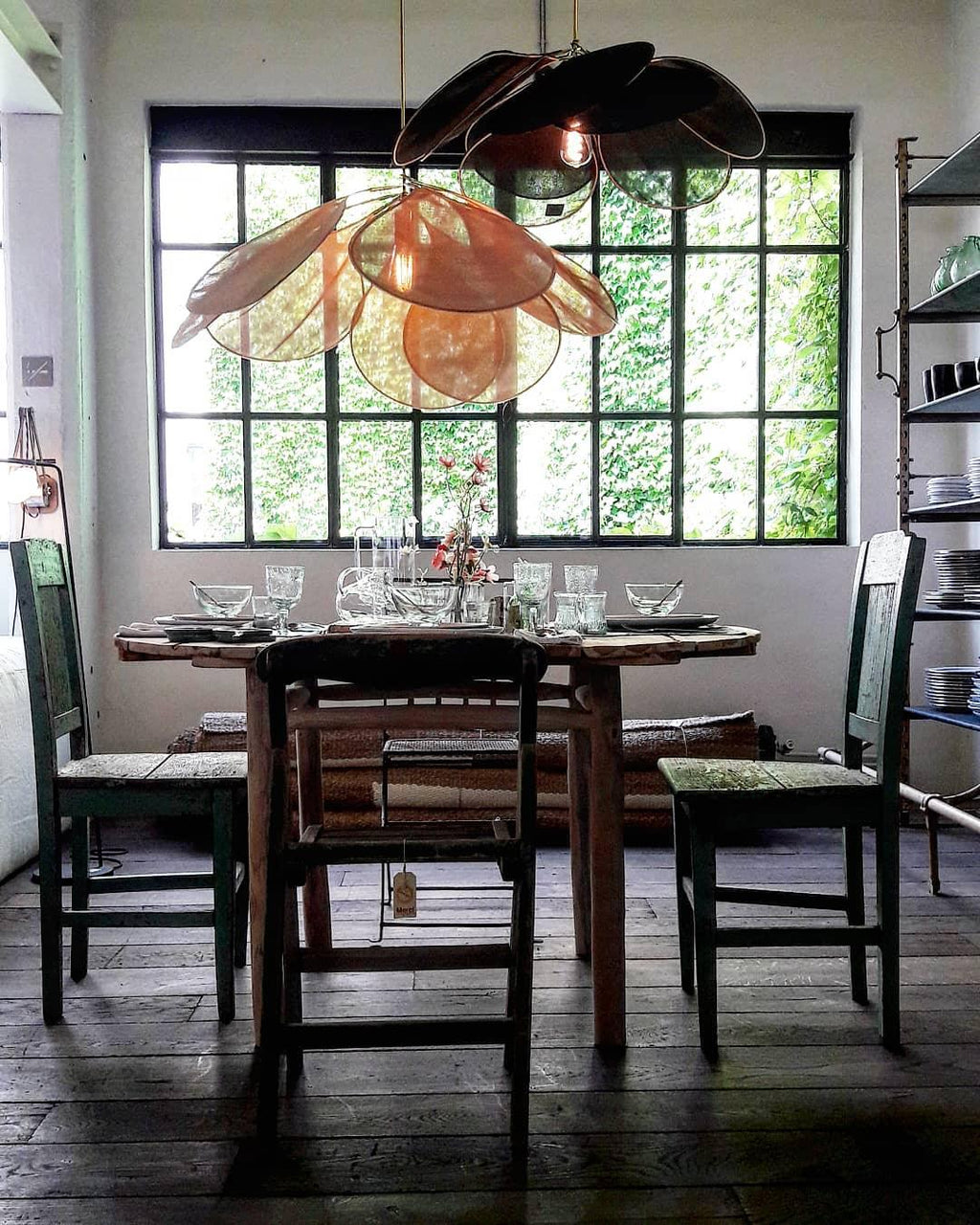 Two of these Clérachic pendant lamps, one dark bronze and one copper, hang above a rustic dining table beside tall factory-style windows.