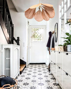 This Clérachic pendant lamp in copper-toned petals hangs above a black-and-white patterned tile floor near a staircase.