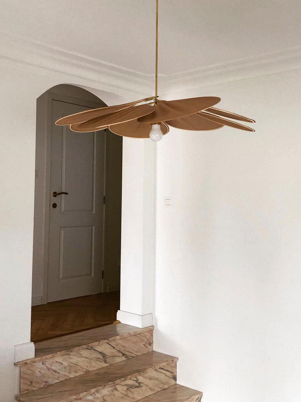 This Clérachic pendant lamp in tan petals hangs in a hallway beside an arched doorway leading to a staircase.
