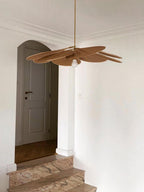 This Clérachic pendant lamp in tan petals hangs in a hallway beside an arched doorway leading to a staircase.