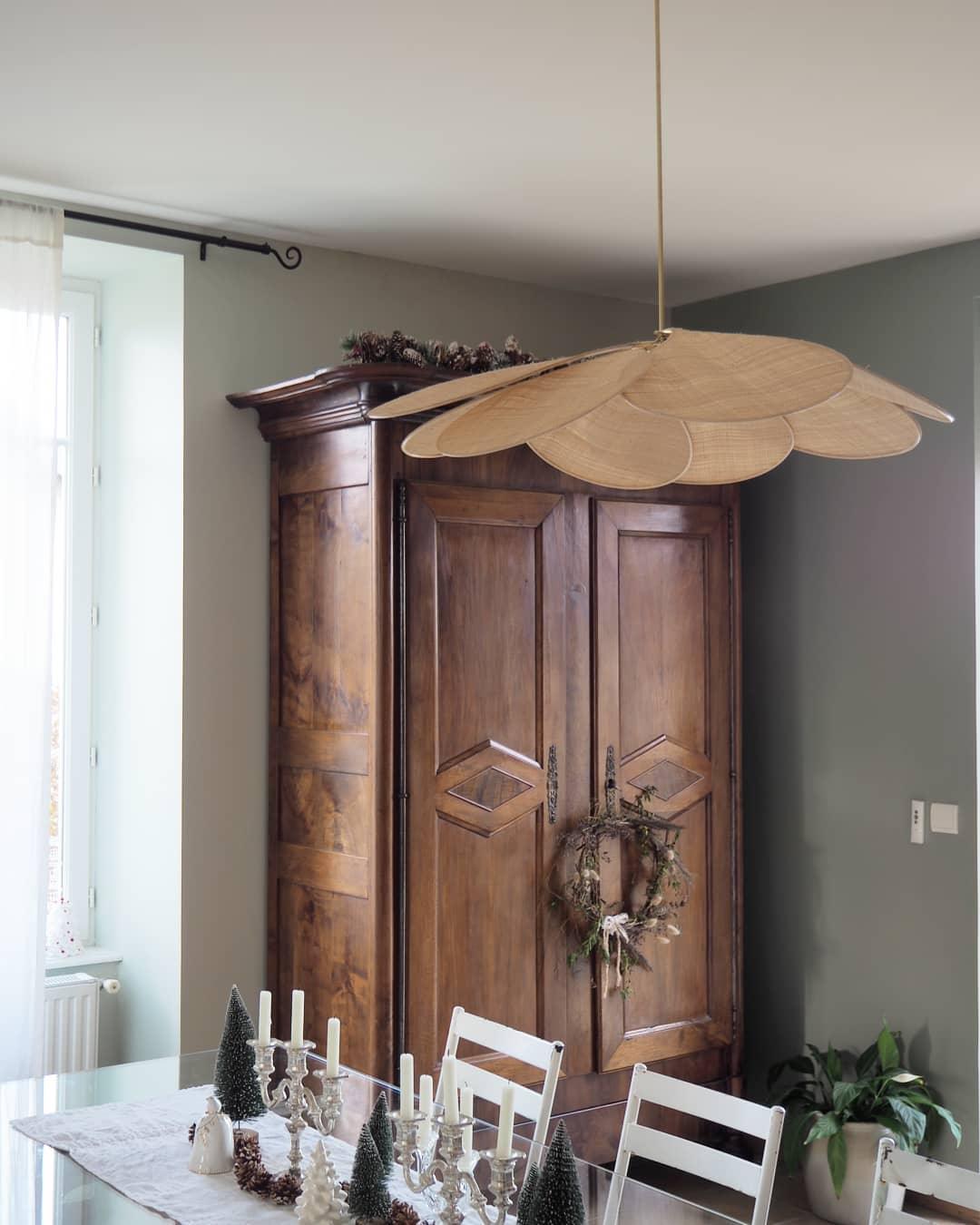 This Clérachic pendant lamp in tan petals hangs above a wooden dining table set for the holidays in front of an antique armoire.