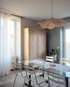 This Clérachic pendant lamp in tan petals hangs above a glass-top dining table near a rustic wooden armoire.