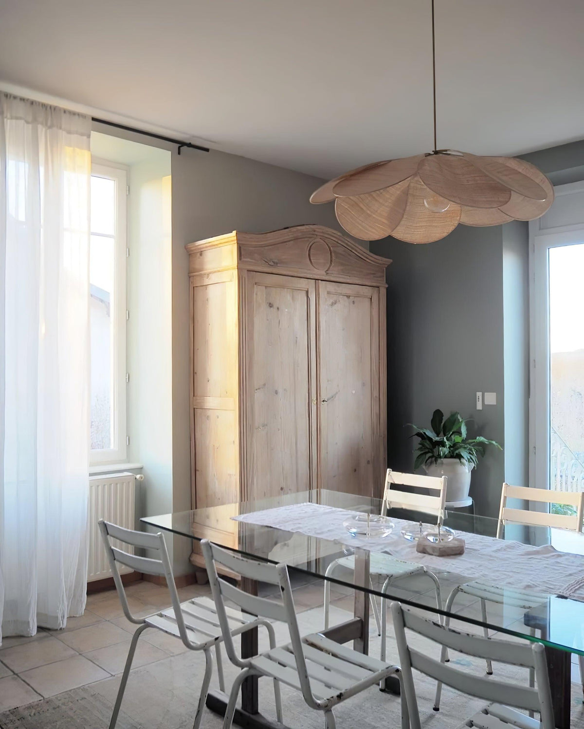This Clérachic pendant lamp in tan petals hangs above a glass-top dining table near a rustic wooden armoire.