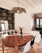 This Clérachic pendant lamp in tan petals hangs above a wood parquet dining table against black-and-white floral wallpaper.