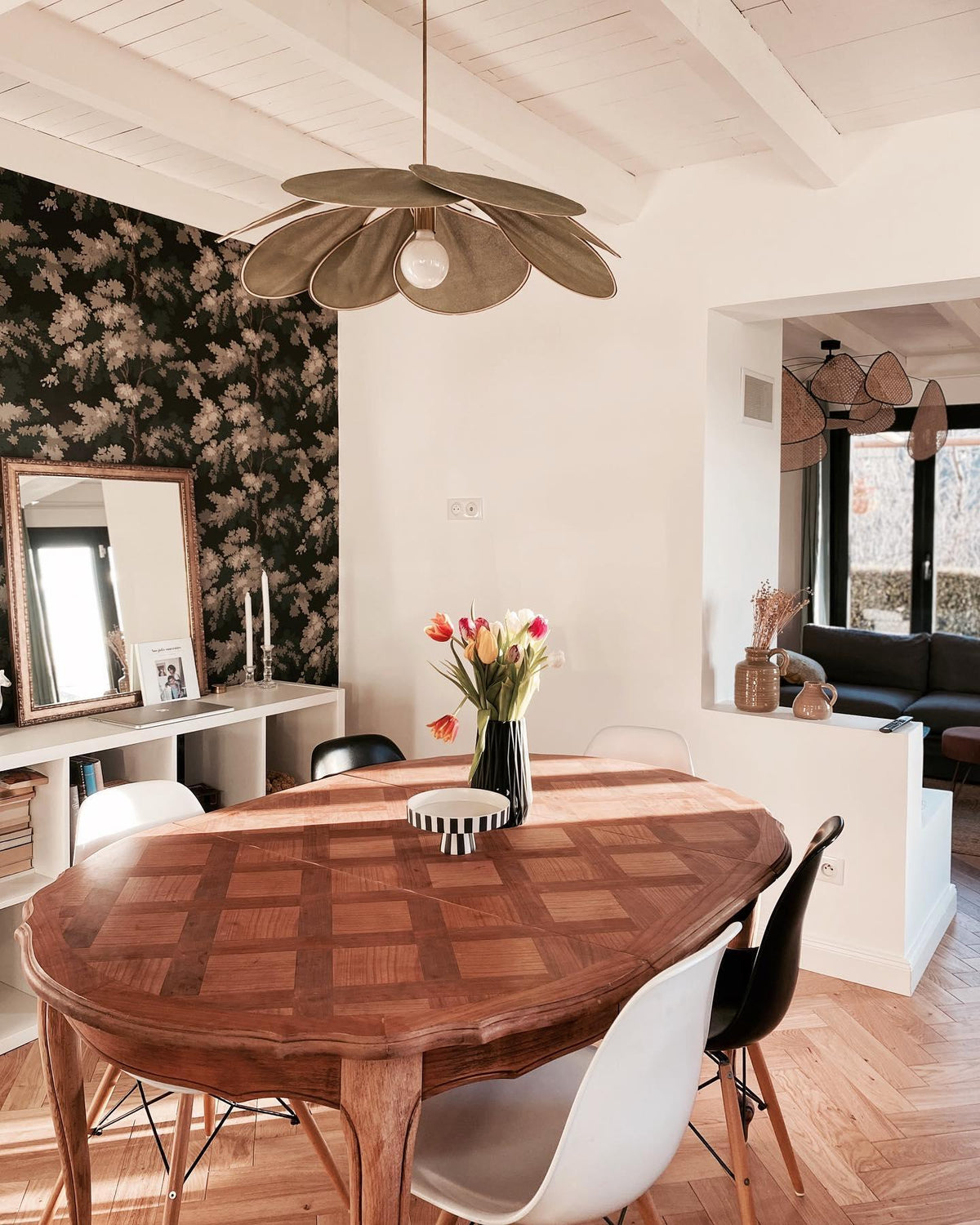 This Clérachic pendant lamp in tan petals hangs above a wood parquet dining table against black-and-white floral wallpaper.