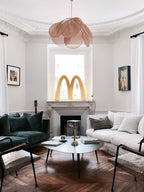 This Clérachic pendant lamp in tan petals hangs in a living room with a dark green velvet sofa and a marble fireplace.