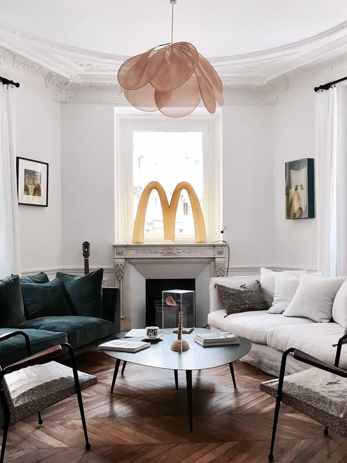This Clérachic pendant lamp in tan petals hangs in a living room with a dark green velvet sofa and a marble fireplace.