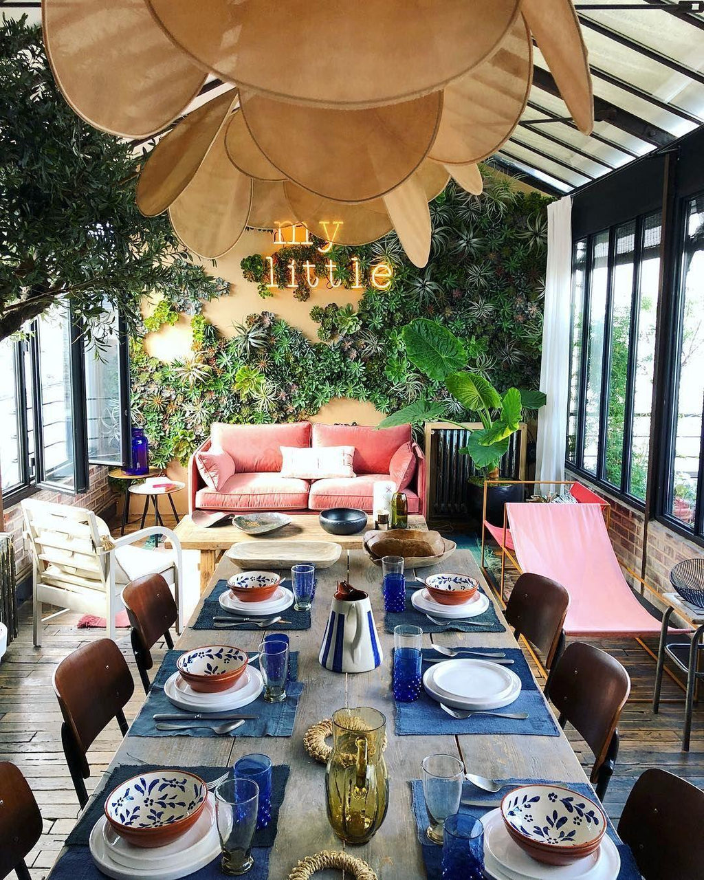 This Clérachic pendant lamp in tan petals hangs over a table set for lunch in a plant-filled sunroom with a coral sofa.