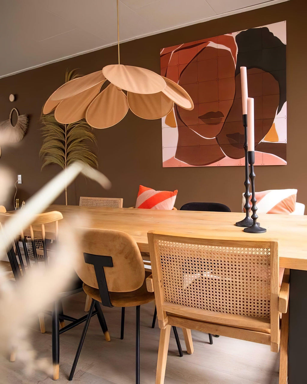 This Clérachic pendant lamp in tan petals hangs above a wooden dining table beneath a colourful portrait painting on an olive wall.