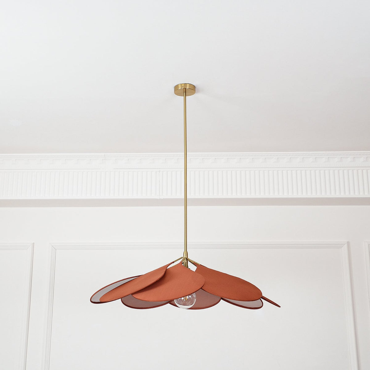 This Clérachic pendant lamp in terracotta petals hangs from a plain white ceiling with panel moulding, its bulb visible beneath.