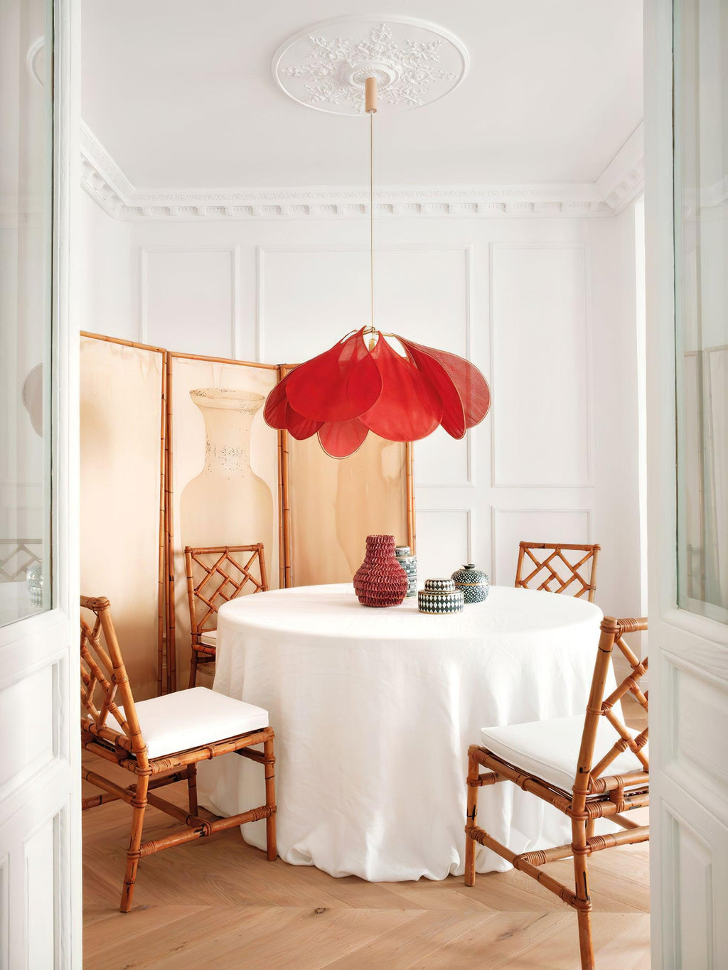 This Clérachic pendant lamp in wine-red petals hangs above a round table dressed in white linen, flanked by bamboo folding screens.
