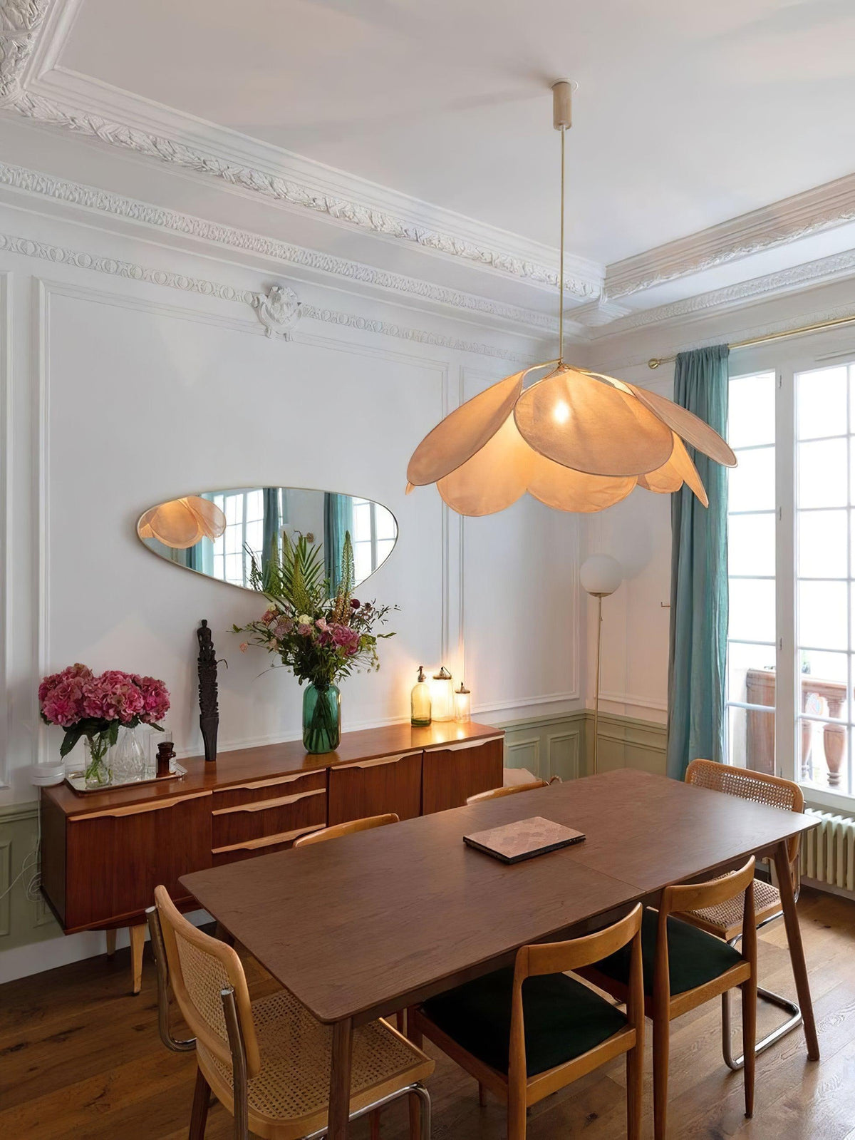 This Clérachic pendant lamp in tan petals hangs above a walnut dining table near an oval wall mirror and a mid-century sideboard.