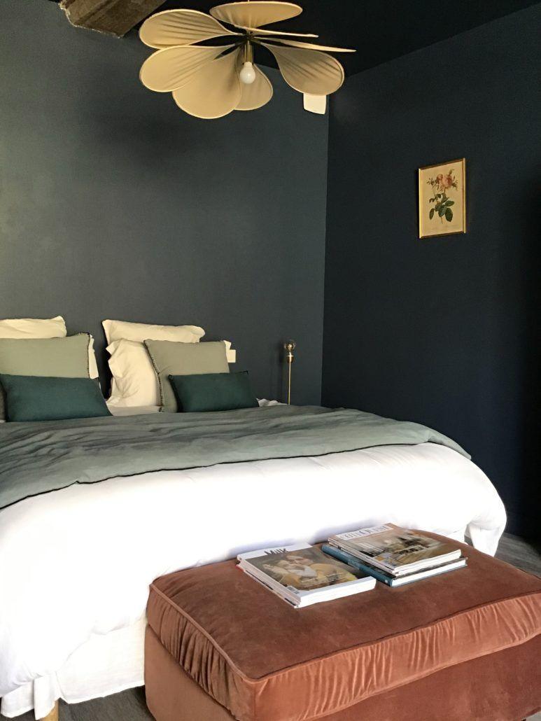 This Clérachic pendant lamp in tan petals hangs in a dark green bedroom with a bed dressed in white and sage linens.