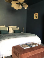 This Clérachic pendant lamp in tan petals hangs in a dark green bedroom with a bed dressed in white and sage linens.