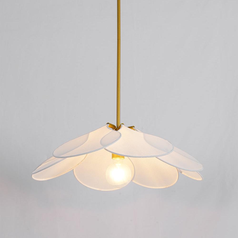 This Clérachic pendant lamp in white petals hangs lit against a plain grey wall, its bulb glowing at the centre.