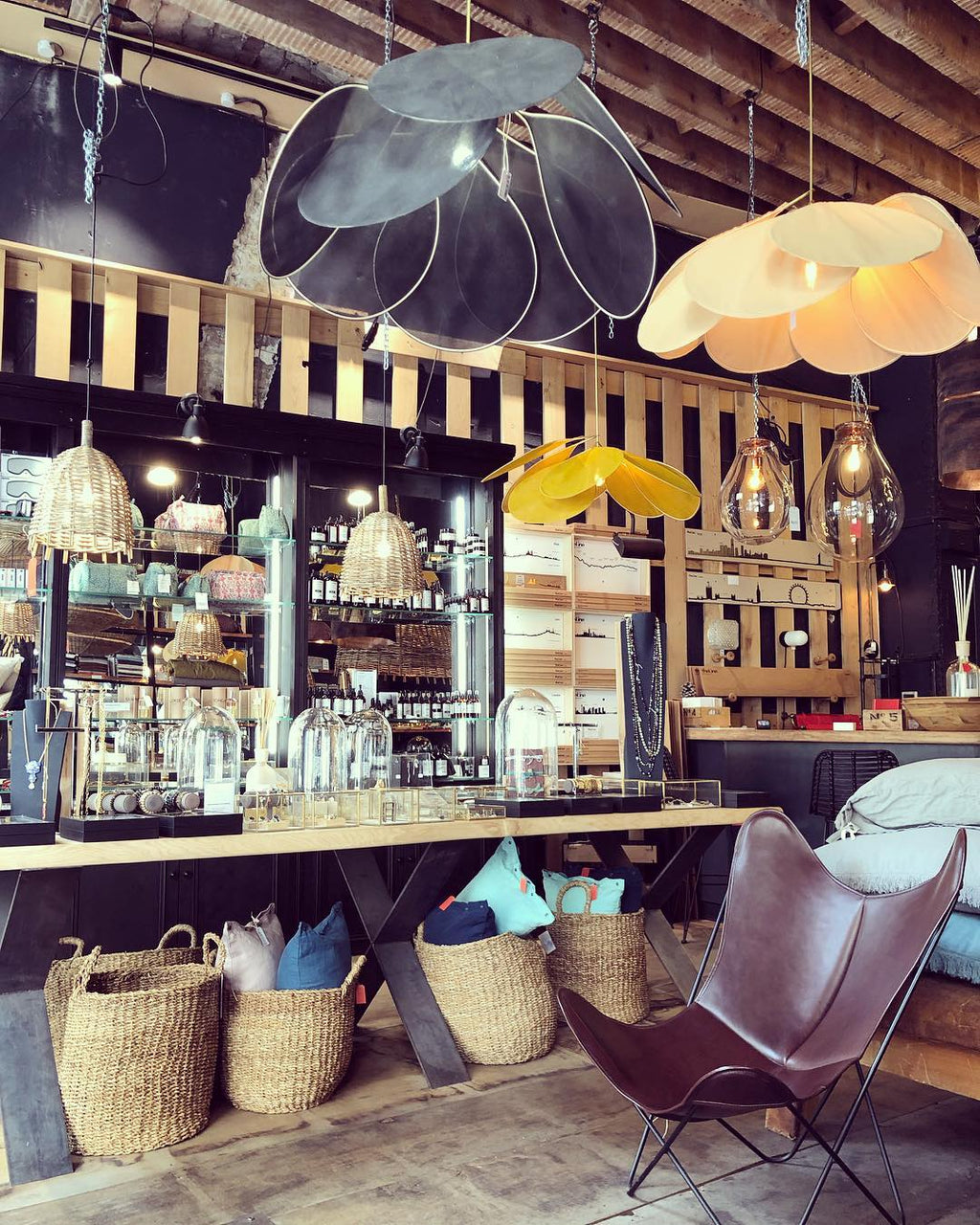 Two of these Clérachic pendant lamps, one dark grey and one tan, hang above a bar counter lined with woven baskets and leather chairs.