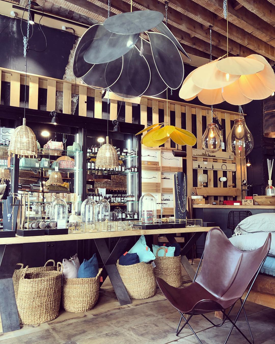 Two of these Clérachic pendant lamps, one dark grey and one tan, hang above a bar counter lined with woven baskets and leather chairs.