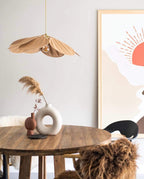 This Clérachic pendant lamp in tan petals hangs beside a round table with dried pampas grass, near a sun-print wall poster.