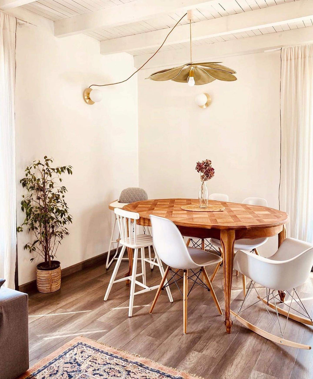 This Clérachic pendant lamp in tan petals hangs above a round wooden table with white chairs in a light-filled dining nook.