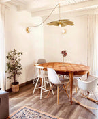 This Clérachic pendant lamp in tan petals hangs above a round wooden table with white chairs in a light-filled dining nook.