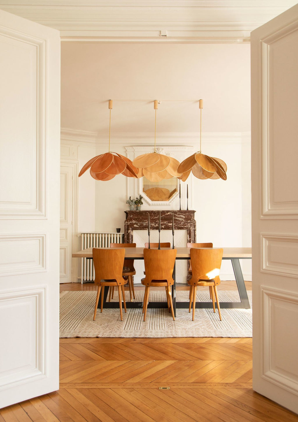 Three of these Clérachic pendant lamps in tan petals hang in a row above a formal dining table with mustard-yellow chairs.