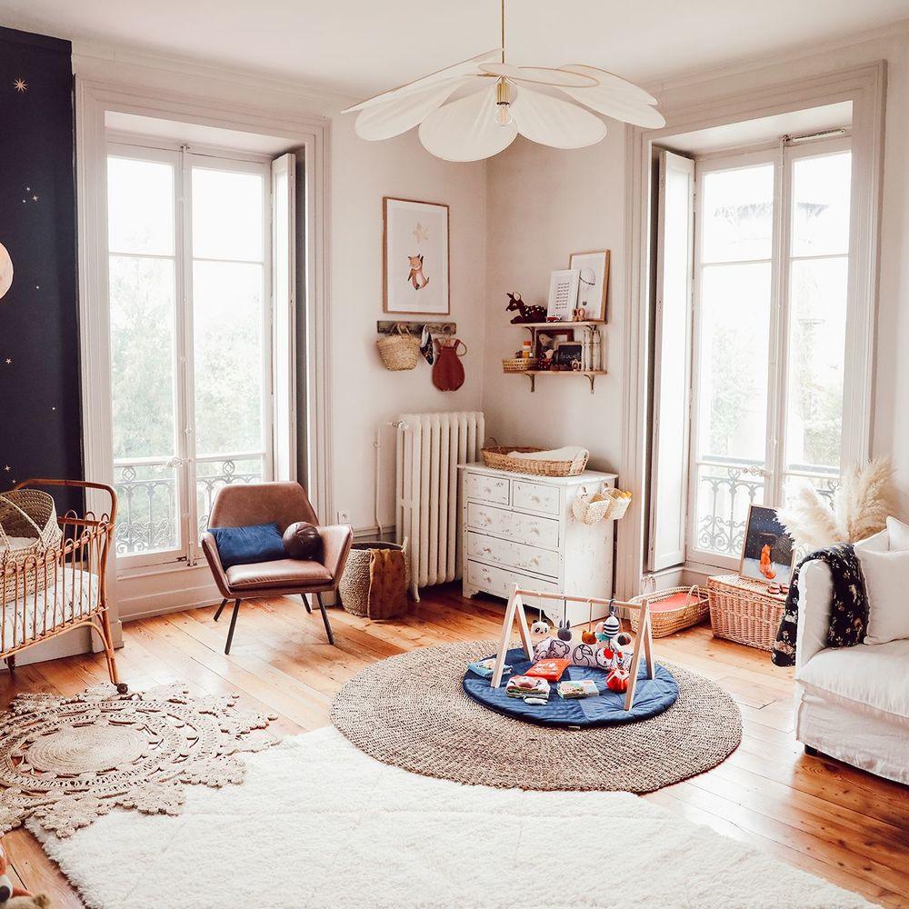 This Clérachic pendant lamp in cream fabric petals hangs in a child's room with a white cot and a woven play rug on the floor.