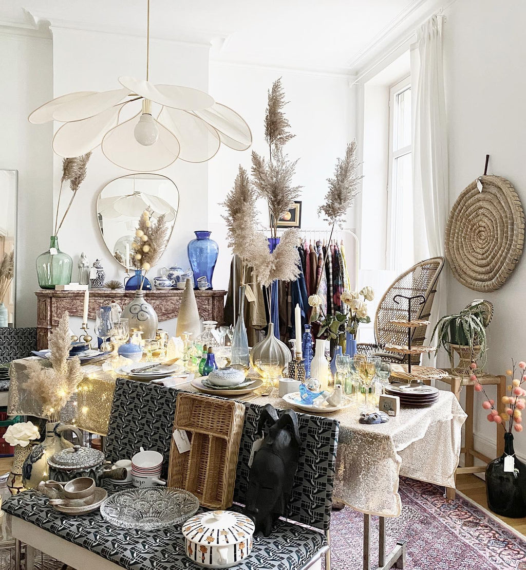 This Clérachic pendant lamp in cream fabric petals hangs above a dining table styled with pampas grass and string lights.
