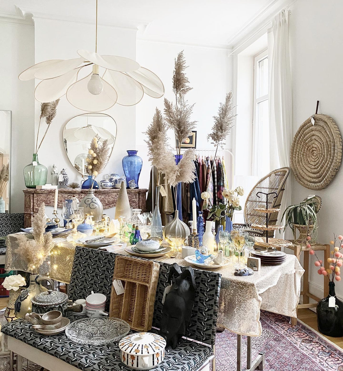 This Clérachic pendant lamp in cream fabric petals hangs above a dining table styled with pampas grass and string lights.