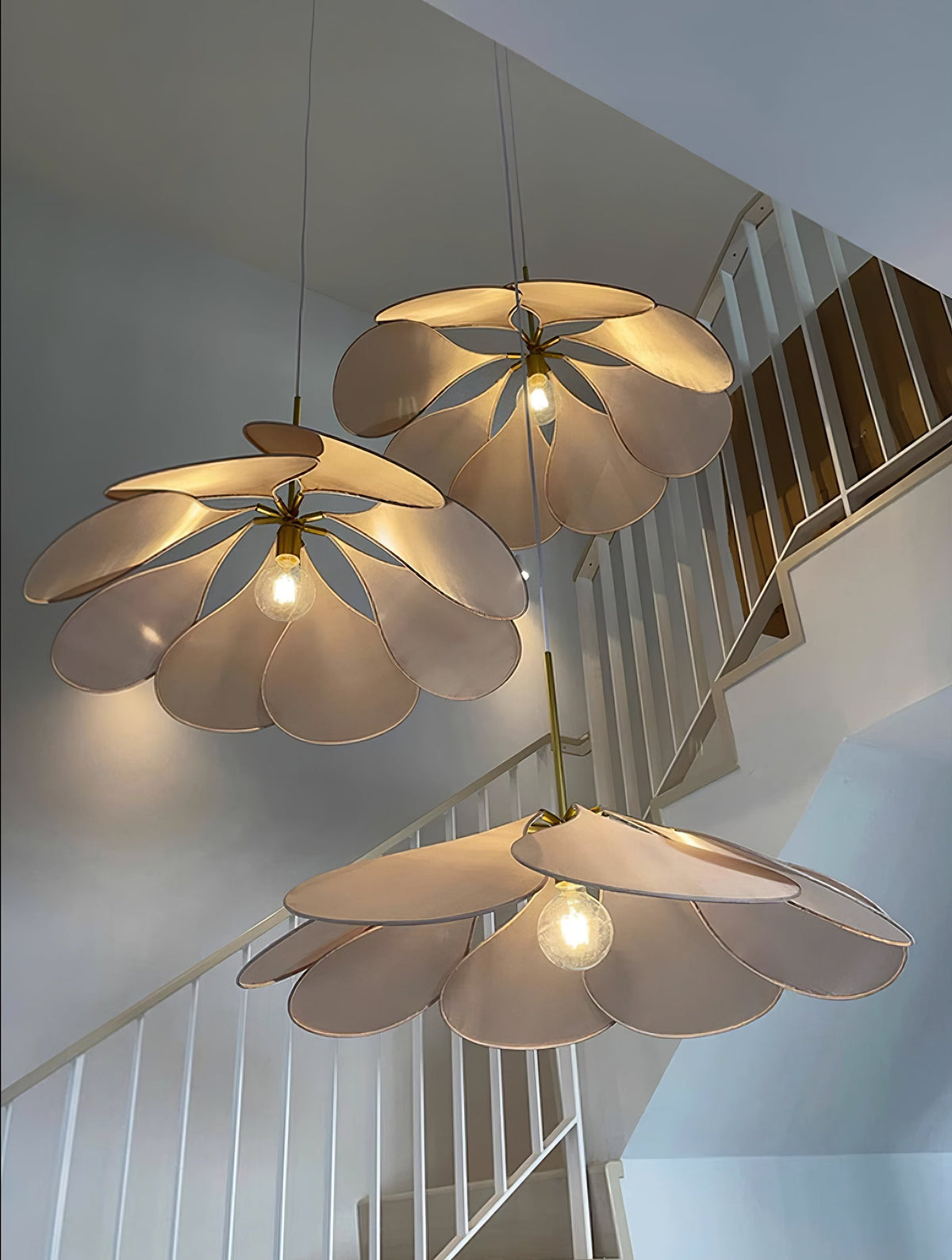 Three of these Clérachic pendant lamps in cream petals hang lit at staggered heights beside a white staircase.