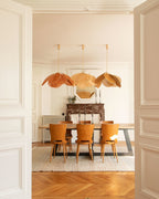 Three of these Clérachic pendant lamps in tan petals hang above a formal dining table with mustard-yellow chairs and a chevron parquet floor.